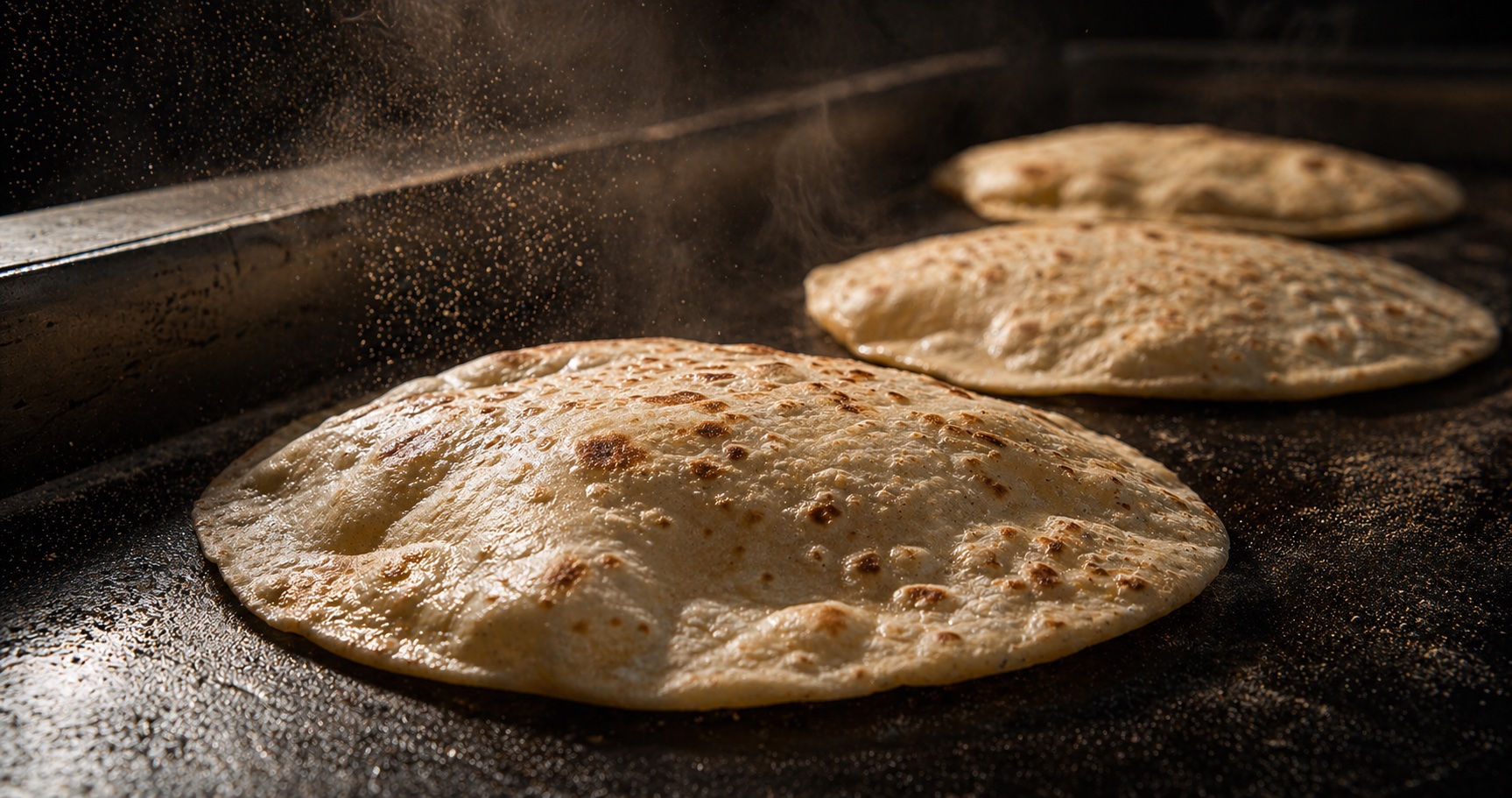 Tres tortillas de harina inflándose sobre un comal de hierro
